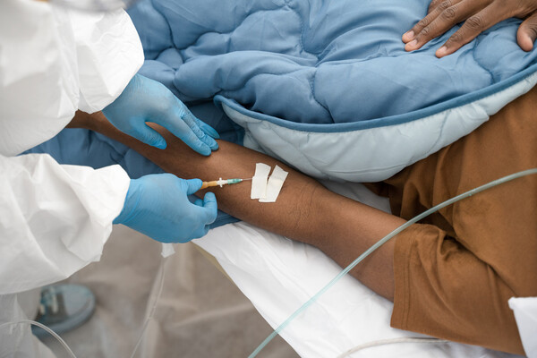 Black patient receiving an injection in the arm by a medical professional.
