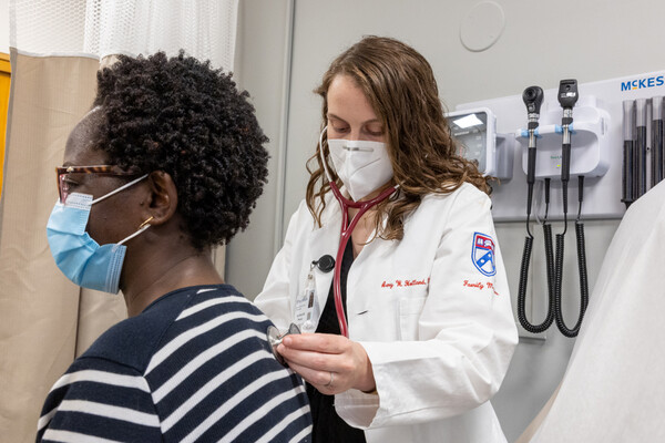 A doctor with a stethoscope checks a patient’s back heartbeat.