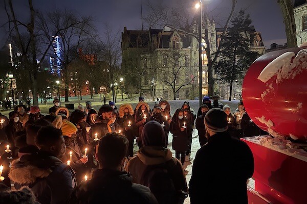 A group of students standing in the snow at night by Penn’s LOVE statue holding candles.