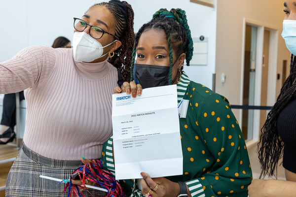 A Penn Med student holds up their Match Day letter standing next to a friend or family member.