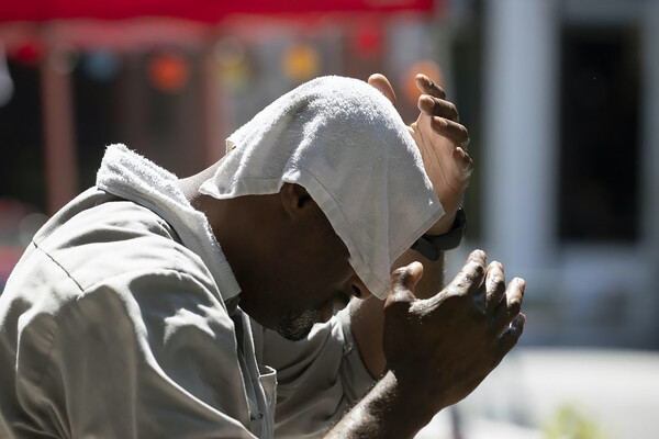 African American person sitting outside cooling their head with a towel.