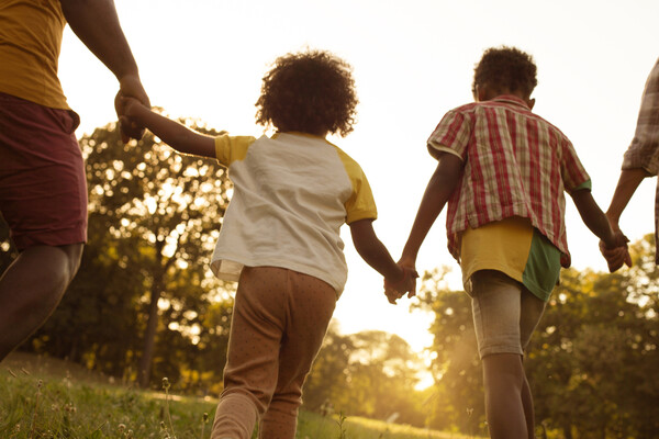 Two children holding hands between two adults in a sunlit grassy area.