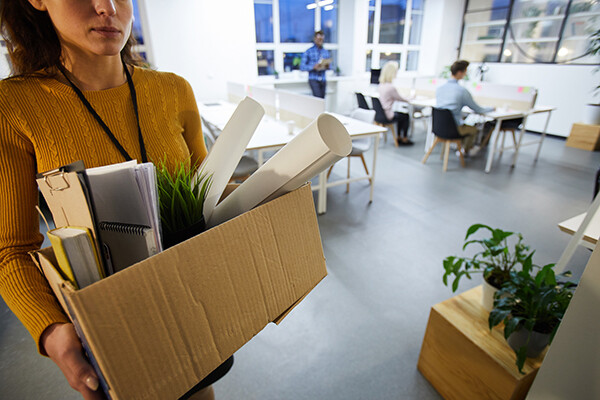 Person carrying a cardboard box of belongings leaving an office.