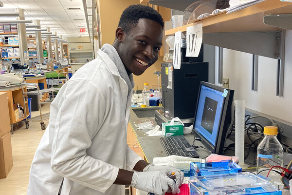A student smiling in a lab wearing a lab coat.