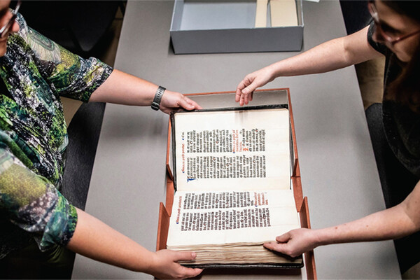 Dot Porter (left) and Andrea Nunez hold a rare book on a table.