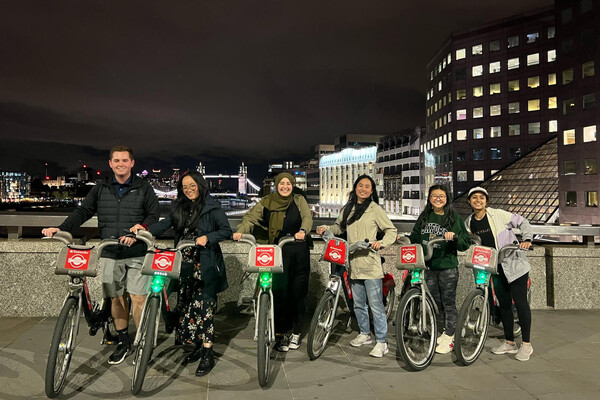 Six Wharton students riding bikes on a bridge at night.