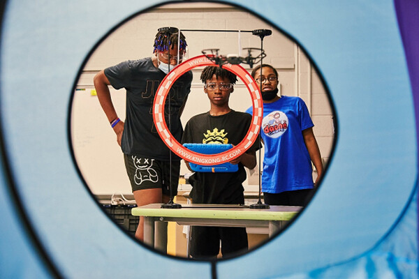 Three students piloting a drone in an elementary school.