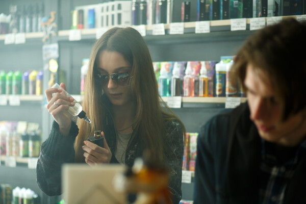 Two teens in a vape shop, one fills their vape cartridge with fluid.