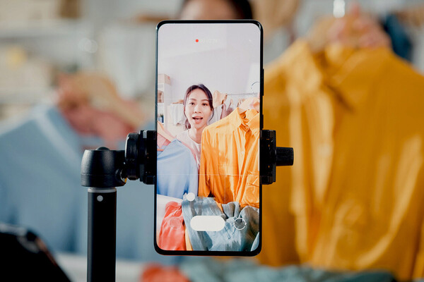 Person selling clothing and filming themselves holding up shirts on a smartphone.