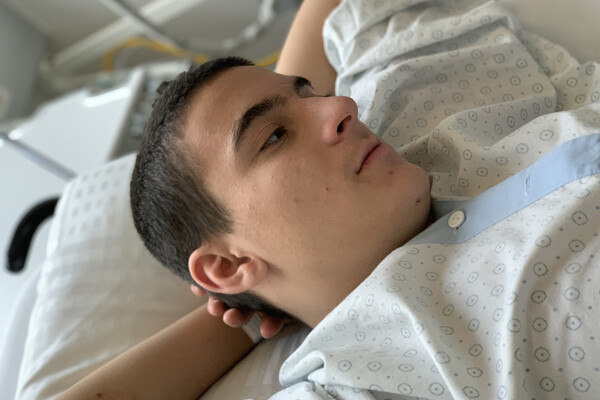 A teenager lying on their back in a hospital bed.