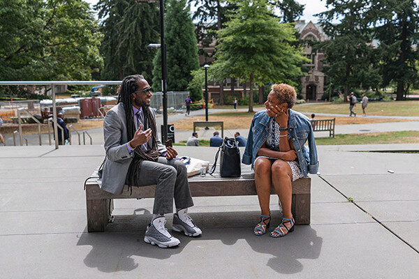 Two people sit outside on a bench talking