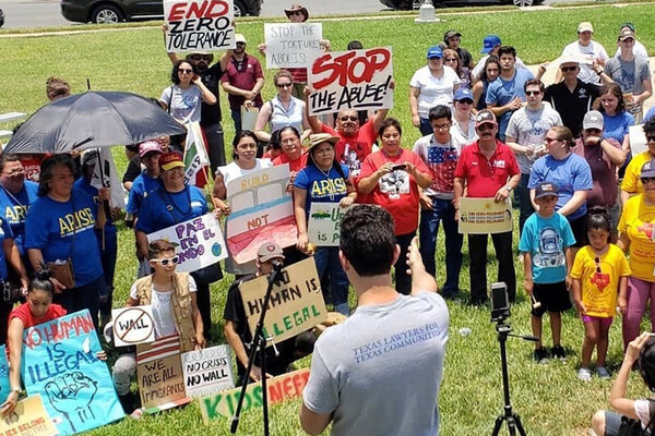 Efrén Olivares speaks to a crowd of people holding signs that say "end zero tolerance," "no human is illegal," and "not one more deportation."