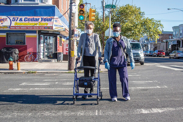 nurse helping elderly person cross the street with a walker