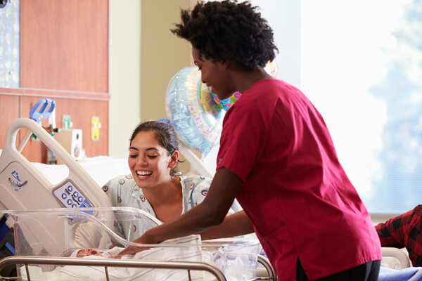A postnatal nurse with a new mother in a maternity ward tending to a newborn.