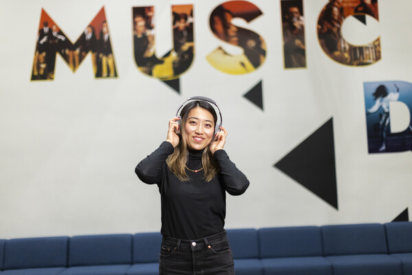 Person holding headphones in front of mural that reads 'Music'