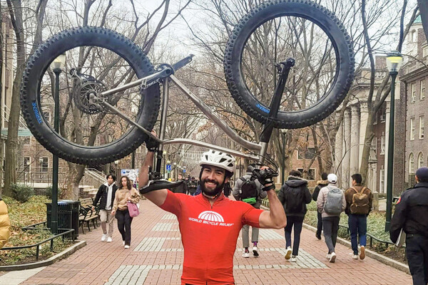 Ryan Torres holds his mountain bike aloft on Locust Walk in cycling gear.