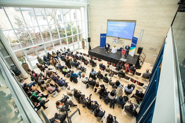 overhead view of room with about 80 chairs mostly occupied and two people on a stage with a big screen behind them