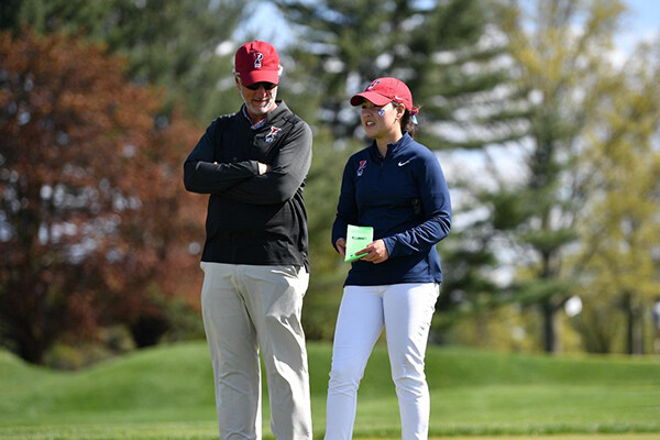 Mark Anderson, left, stands with his arms folded while speaking to a person wearing a red hat and a blue Penn pullover.