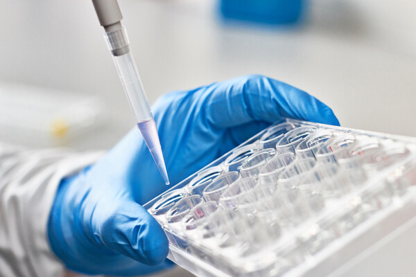 Closeup of a pipette and a tray of vials held by a gloved hand.