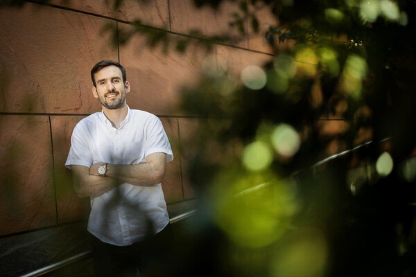 Nick Martin stands against a red sandstone building, with foliage in the foreground