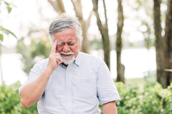 Senior citizen in nature holding their head with a headache.