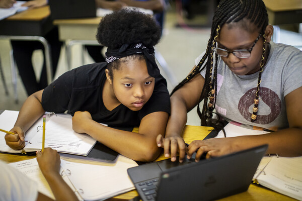 Two high school students at a table looking at a laptop.