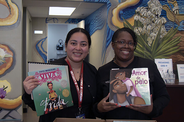 Two people holding up children’s books written in Spanish.