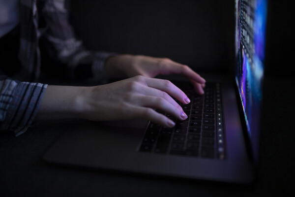 Hands typing on a laptop in the dark.