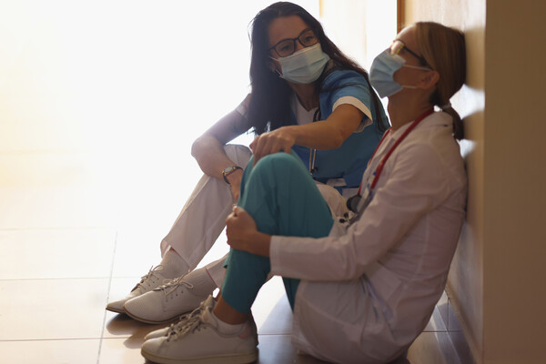 Two masked medical professionals seated on the floor looking burned out.
