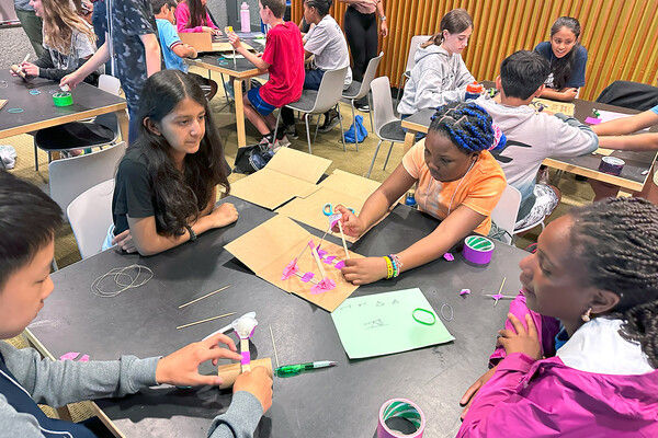 Groups of middle school students working on projects at tables.