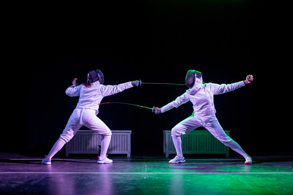 Two actors in fencing gear performing on stage.