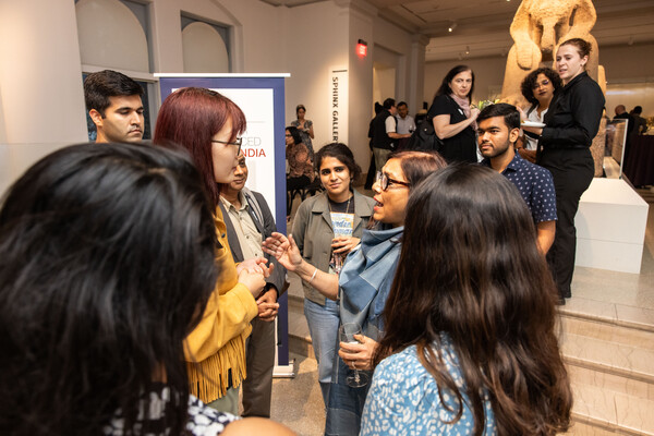 A group of people cluster around Mira Nair at the Penn Museum with the Sphinx in the background.  