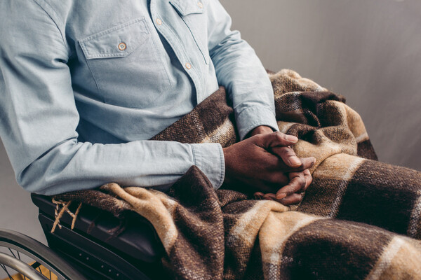 A person in a wheelchair with their hands folded in their lap.