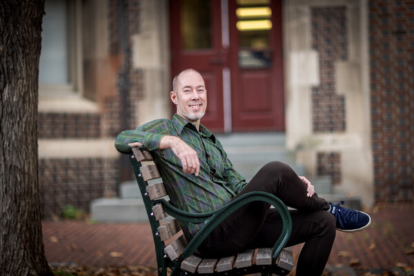 John Donges sitting on a bench in an outside courtyard