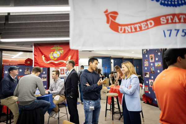 In a room decorated with armed services' flags, pictures of service members, and stars, President Liz Magill talks with Landon Le, a second-year student.