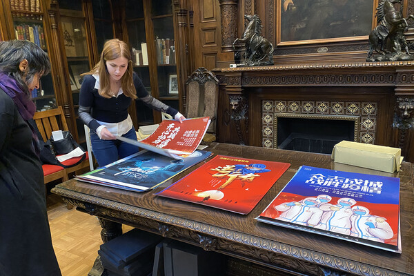 Two people looking at large COVID posters on a table in the Kislak Libary.