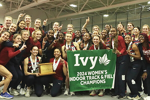Members of the women's track and field team pose with the Indoor Ivy Heps championship banner after winning the competition at Harvard.