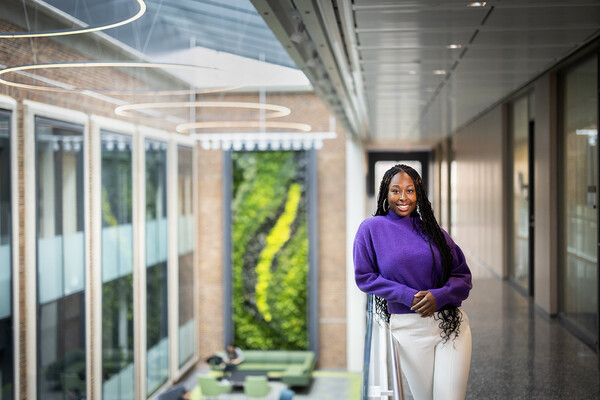 Taussia Boadi stands on the mezzaine of the Wharton Academic Research building, with the lobby seen below and a floor to ceiling piece of art in various shades of green behind her.