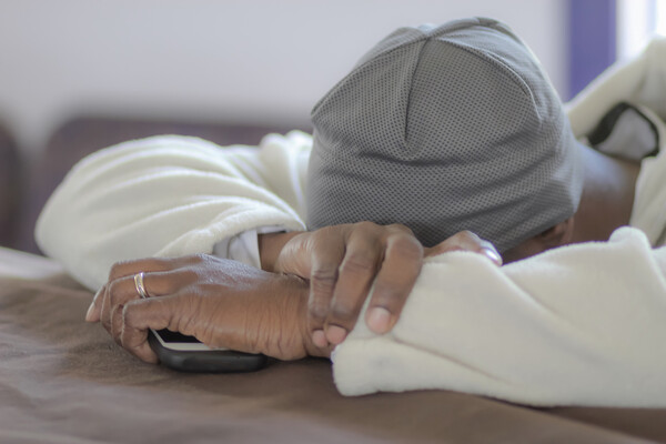 A person resting their head on their folded arms holding a smartphone.