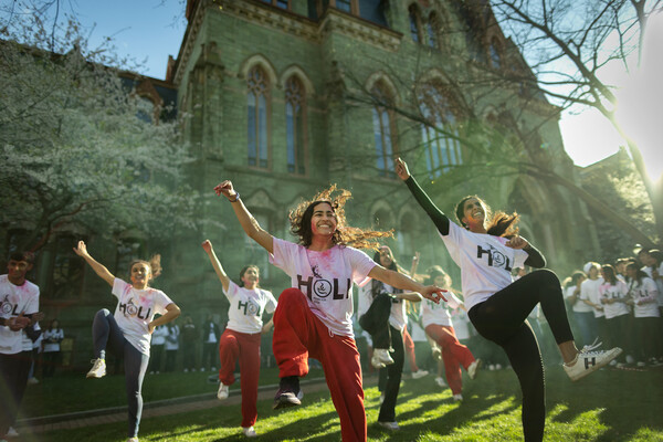 A group of dancers with shirts reading Holi perform in front of College Hall