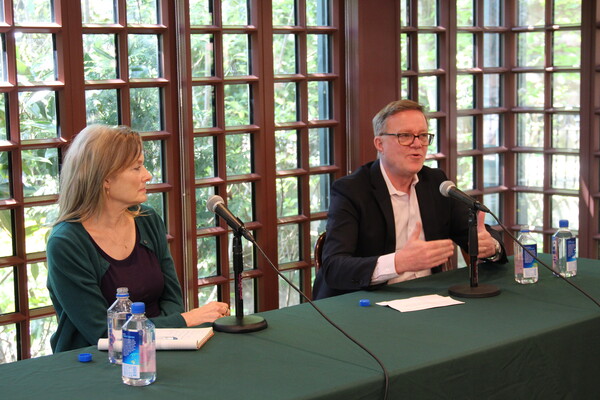 Jennifer Egan and Dennis Culhane sit at a long green table in front of the windows at Kelly Writers House