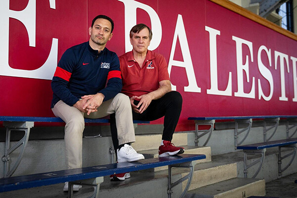 Matt Valenti, left, and Roger Reina sit on a blue bleacher bench inside the Palestra.
