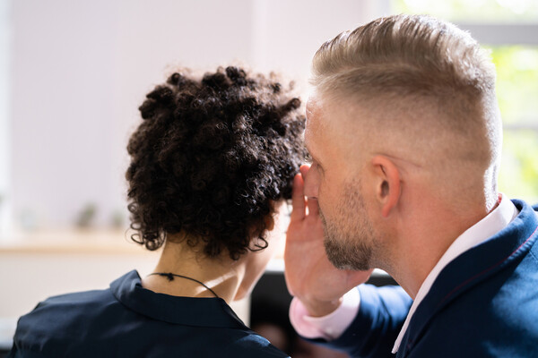 One person whispers in the ear of another.