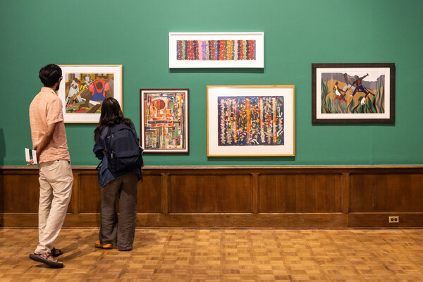 two people looking at five artworks on a wall