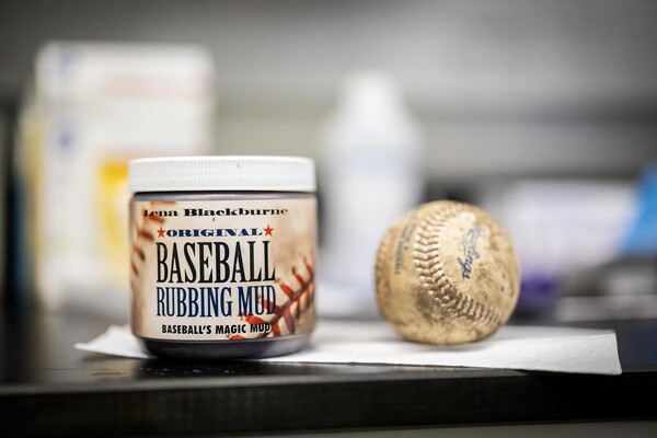  A jar of Lena Blackburne Baseball Rubbing Mud sits on a table beside a muddy, dirty baseball. 