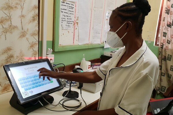 Health care worker in mask stands at tablet with electronic medical record system.