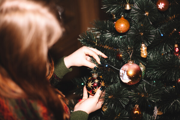 A person putting ornaments on an artificial Christmas tree.