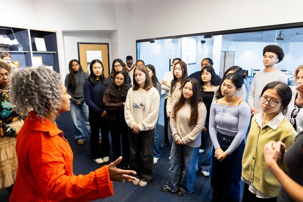 Students standing listening to a person speaking.