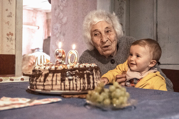 An elderly person holding a baby while blowing out candles on a birthday cake.