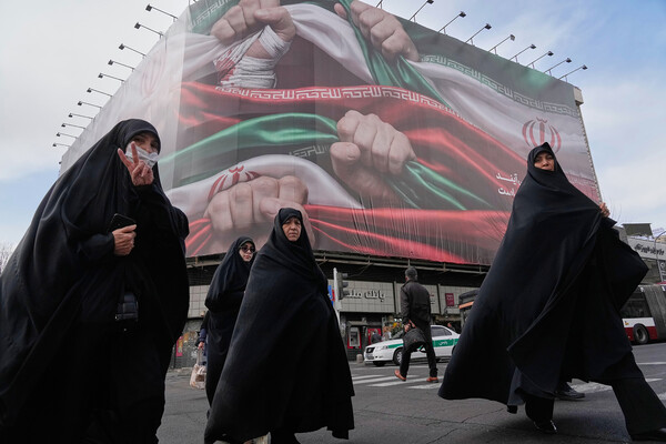 Four women walk through Tehran underneath a billboard.
